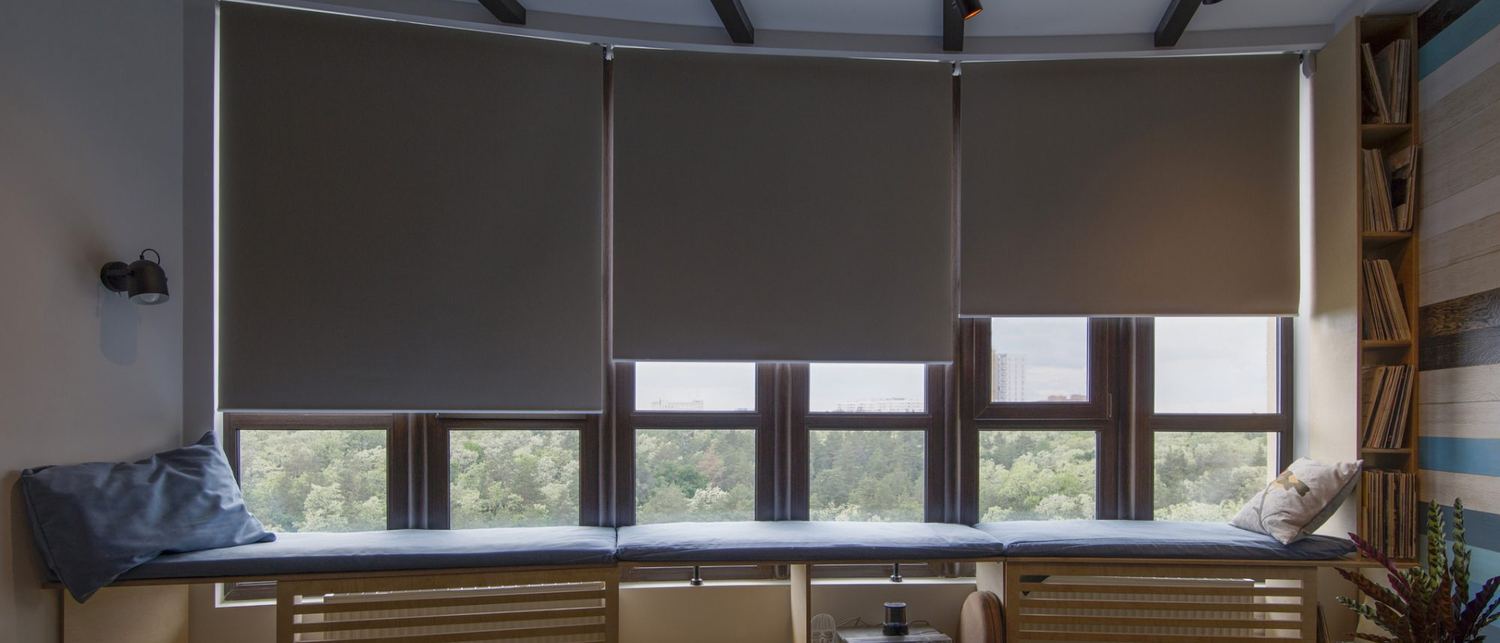 A living room with roller blinds drawn across a wide bay window, evening light on the walls