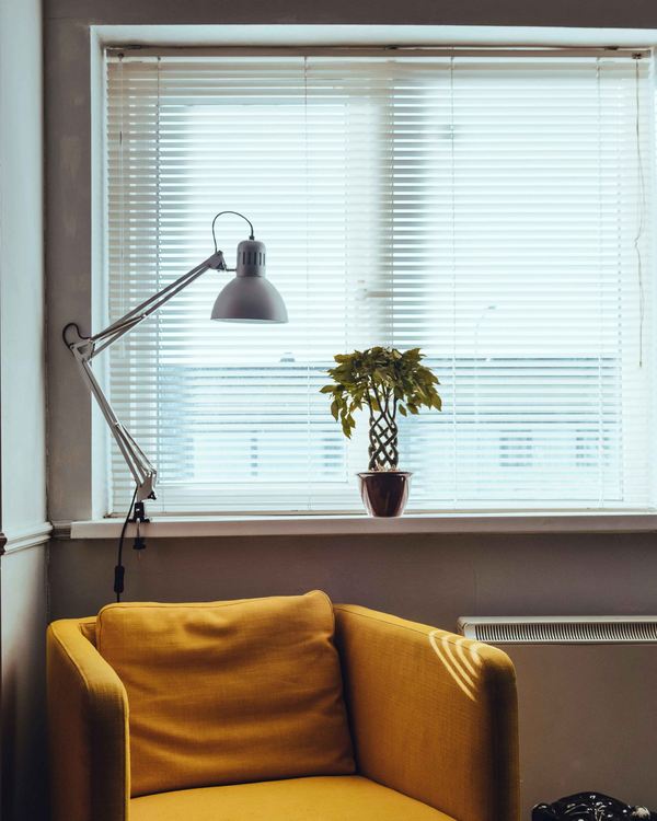 A chair beside a window dressed with slatted blinds casting striped light