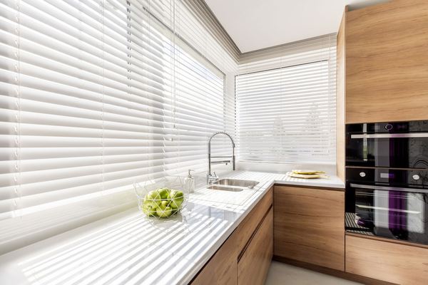 Kitchen window dressed with white blinds above a run of units