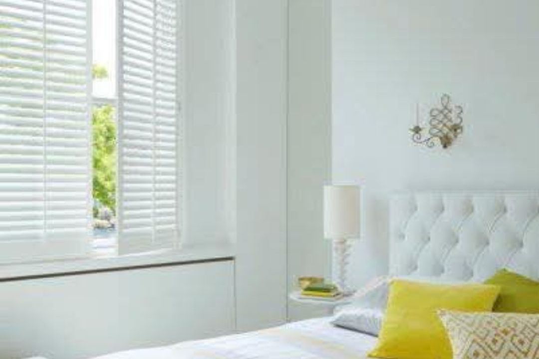 White plantation shutters in a bright bedroom, louvres angled to soften the daylight