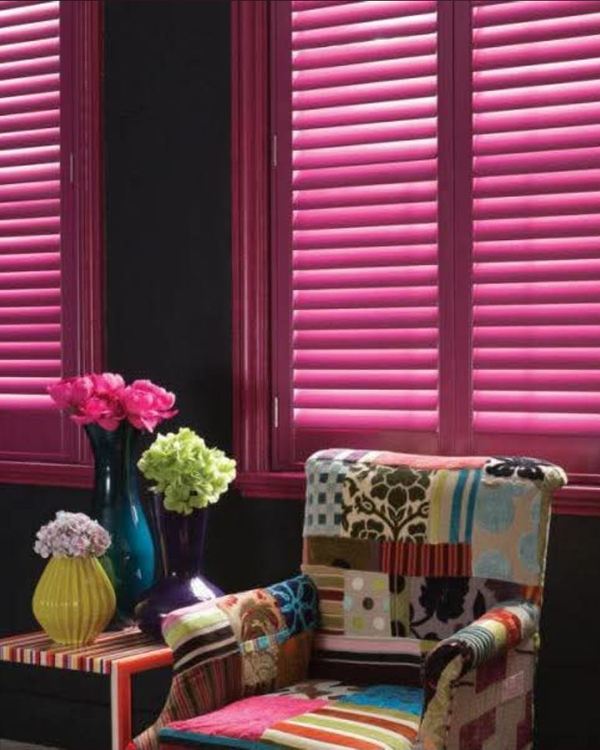Bold pink shutters against a dark wall beside a patterned armchair