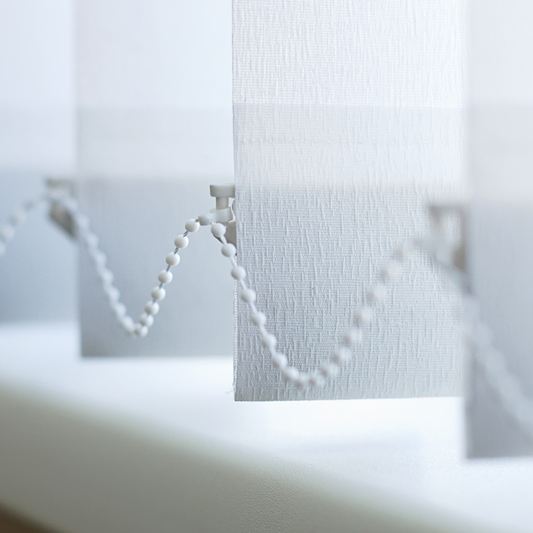 White vertical blind louvres drawn across a wide window